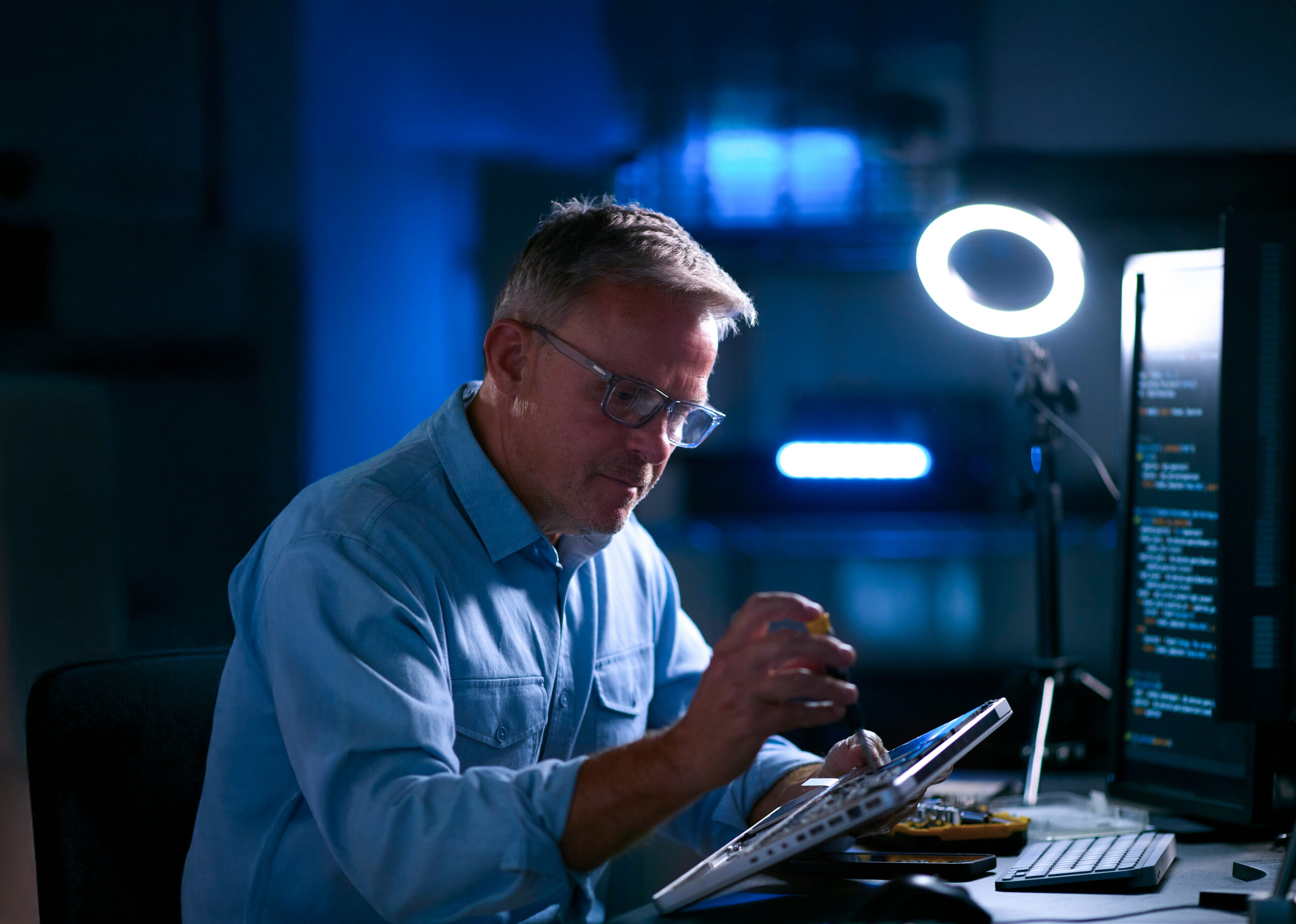 Mature Male Electronics Expert Repairing Laptop In Workshop With