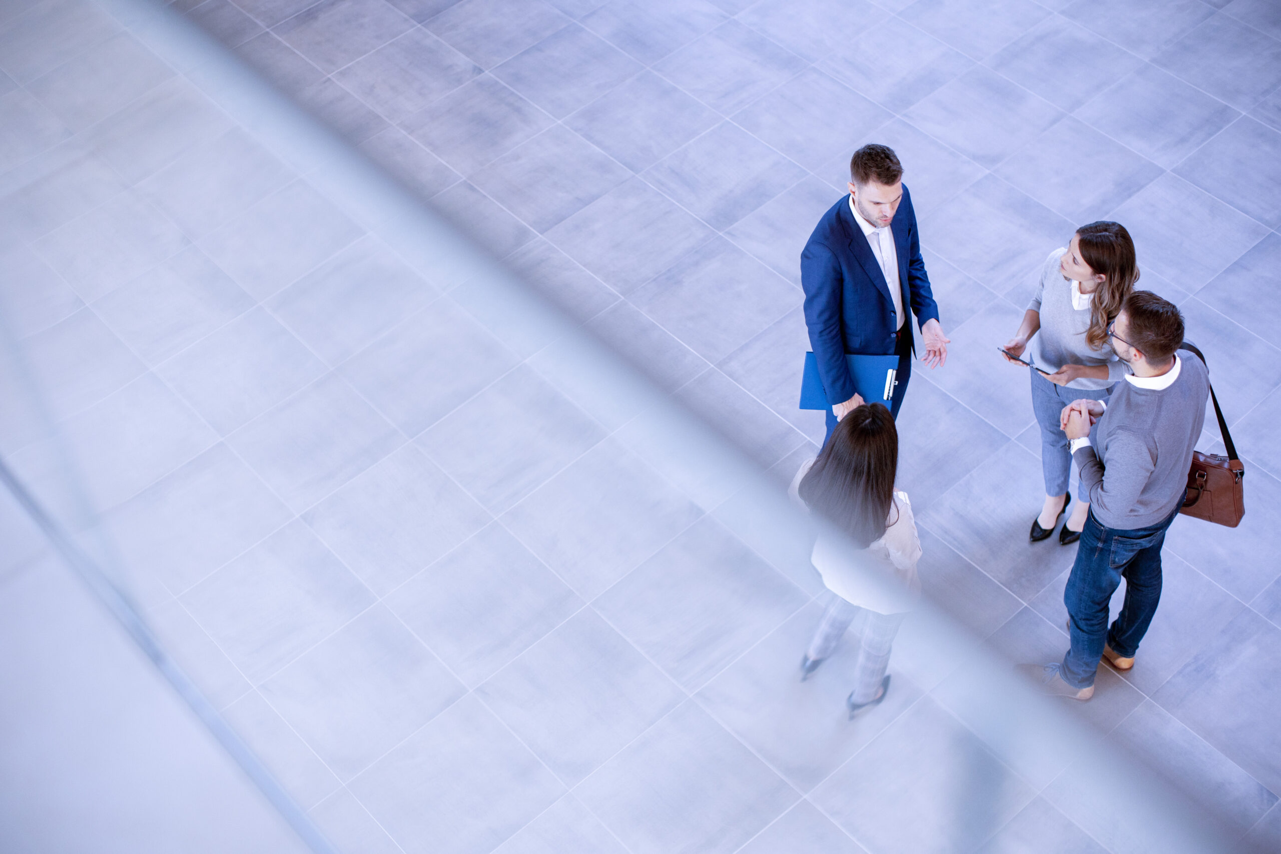 Four people standing in a tiled open space engaged in conversation, with two men and two women facing each other.